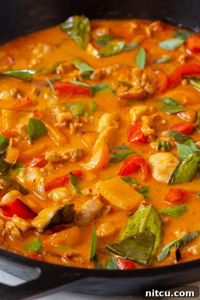 A vibrant bowl of Thai Panang Chicken Curry, garnished with fresh basil, served in a cast iron pan