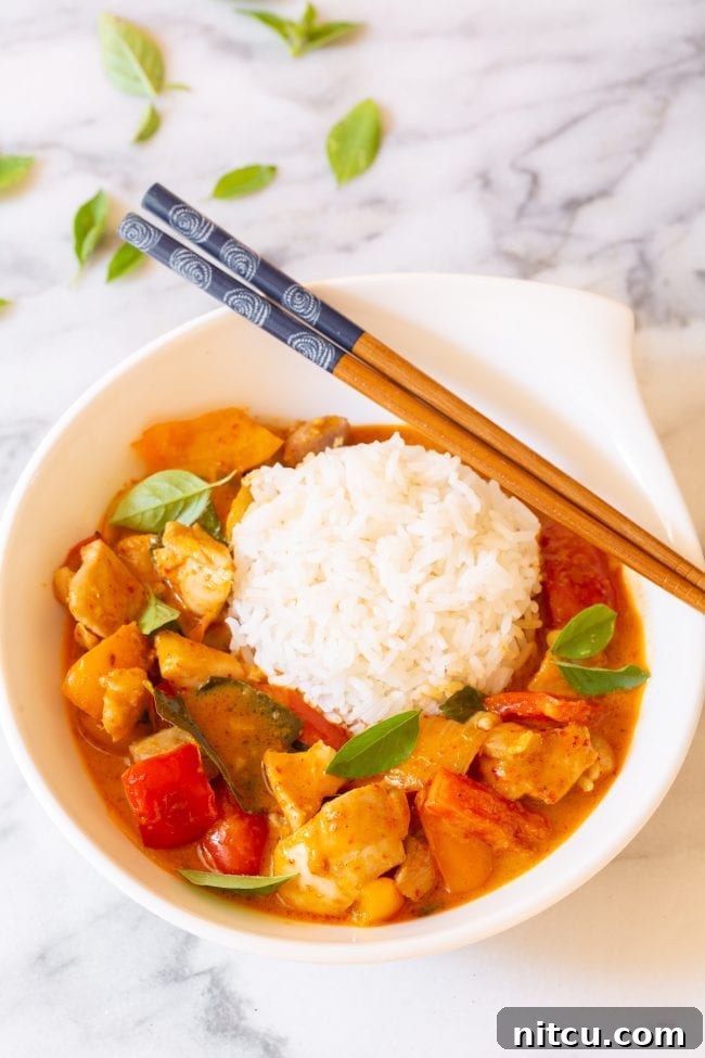 A beautifully plated bowl of Best Thai Curry - Panang Chicken with white rice and fresh basil, ready to eat.