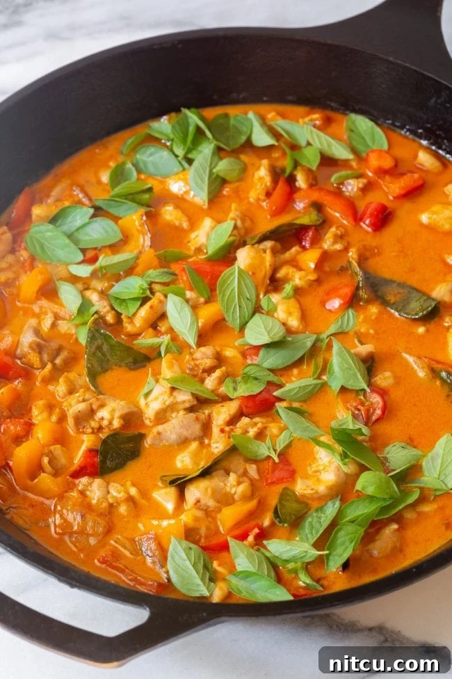 Best Thai Chicken Curry simmering in a skillet with fresh basil leaves on top, creating an inviting aroma.