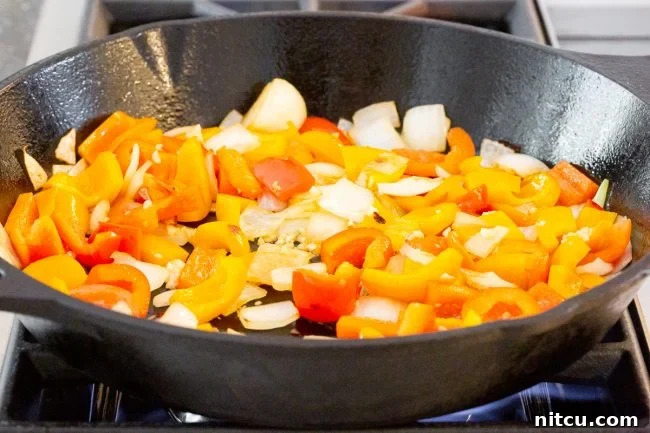 Chicken and colorful bell peppers being sautéed in a skillet, building the flavor foundation.