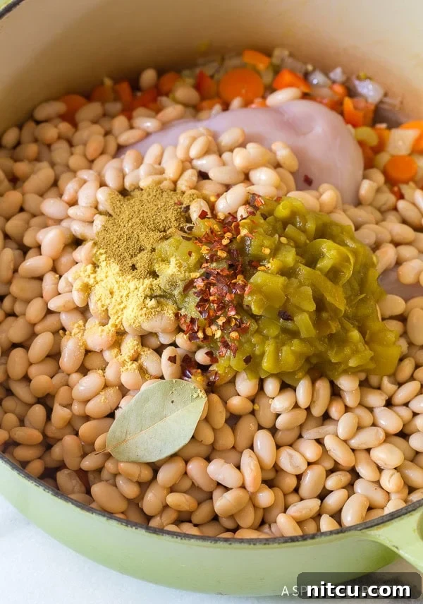 Ingredients for white bean chicken soup neatly arranged in a green soup pot before cooking.