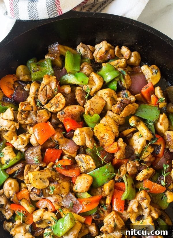 A top-down view of a sizzling skillet brimming with cooked Croatian chicken and an array of colorful vegetables.