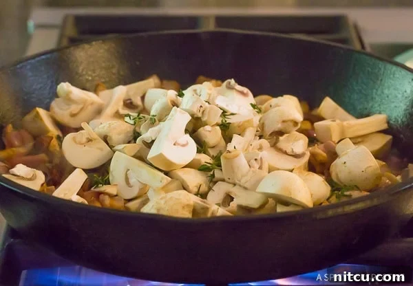 Earthy button mushrooms being sautéed in a hot skillet, beginning to soften and release their flavors.