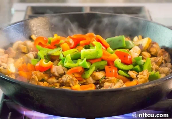 Charred bell peppers being tossed back into a skillet with fully cooked chicken and other vegetables, blending flavors.