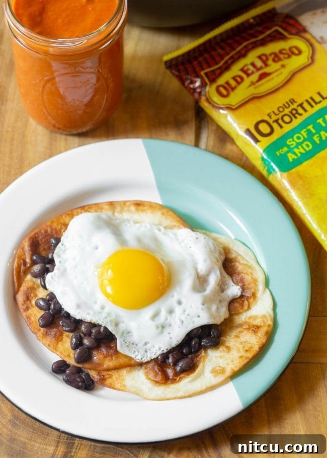 Stacked fried tortillas on a plate with fried egg and beans, ready for sauce.