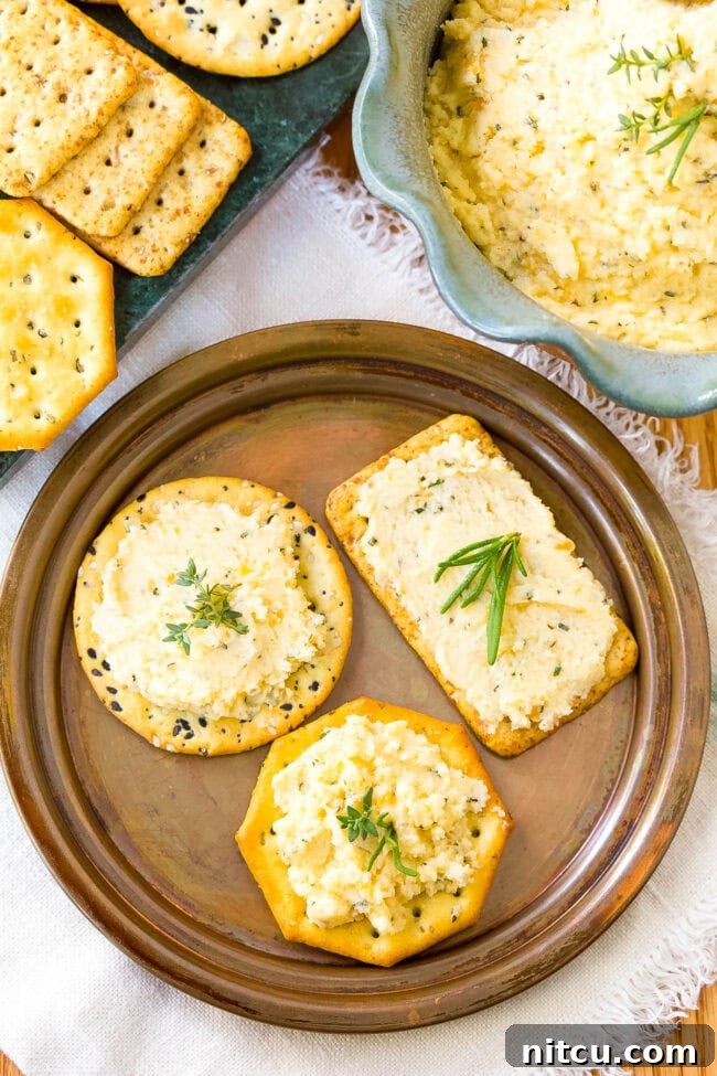 Top-down view of a plate with crisp crackers generously topped with fresh homemade cheese spread and a sprig of fresh rosemary.