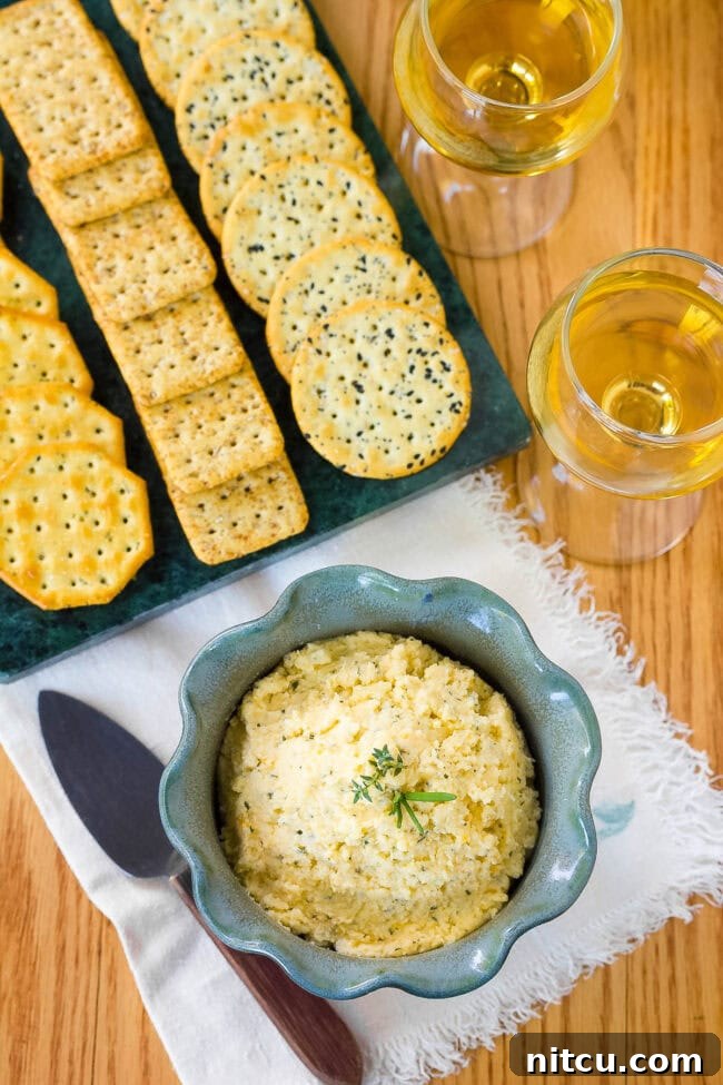 Top-down view of a beautifully arranged spread with homemade cheese dip, an assortment of crackers, and a glass of white wine.