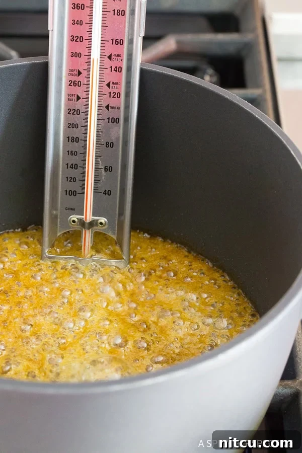 Buttery brown sugar toffee mixture simmering in a saucepan with a candy thermometer showing temperature.