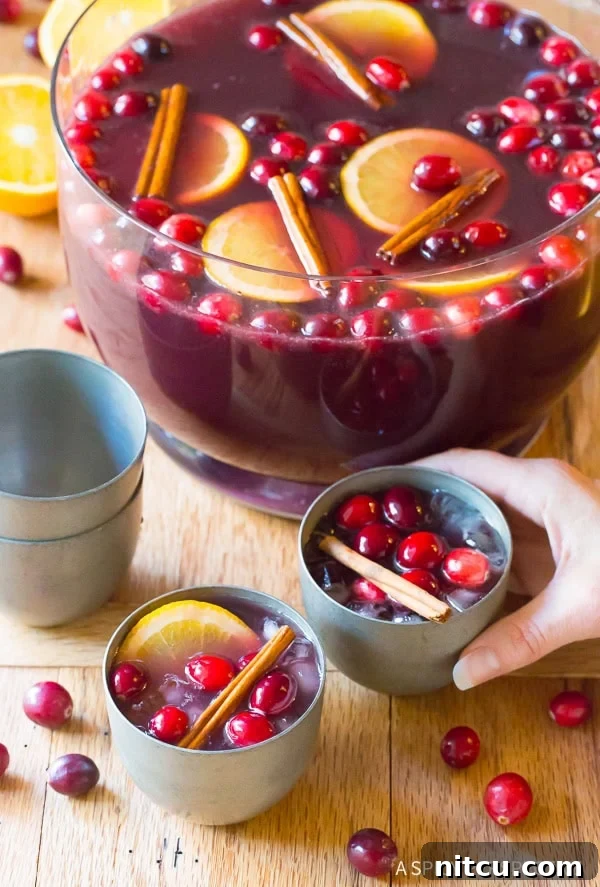 A hand reaching for a glass of the festive Holiday Wine Punch, with the elegant punch bowl brimming in the background, signaling a joyful celebration.
