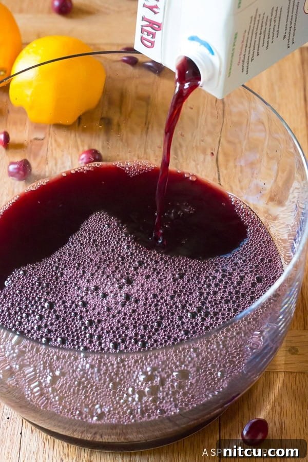 A close-up view of red boxed wine being gracefully poured into a spacious glass punch bowl, illustrating the beginning of crafting our festive wine cocktails.