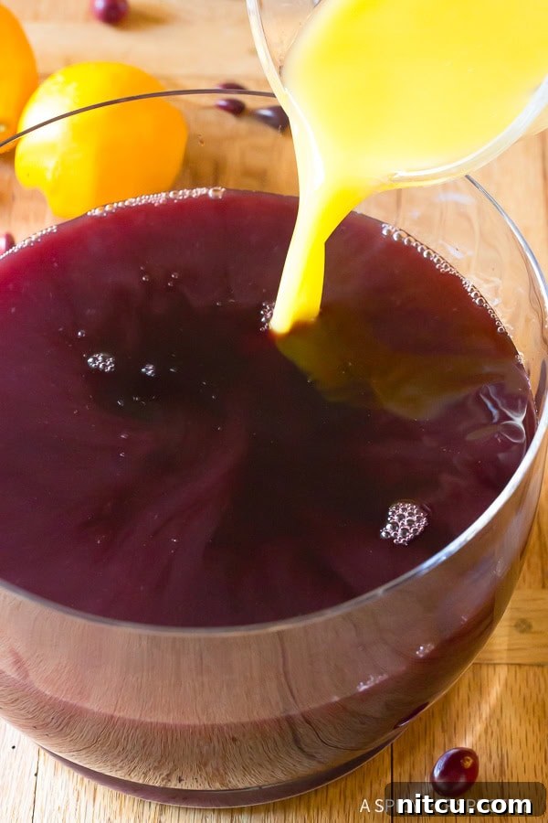 A vibrant stream of fruit juice being added to the red wine already in the punch bowl, showcasing the blend of flavors in the Holiday Wine Punch.