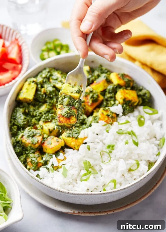 Hand with fork that's picked up a bite of saag paneer.