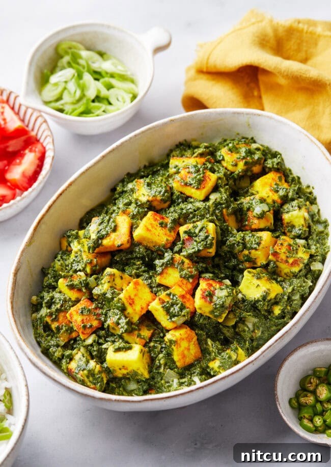 Saag paneer in a serving bowl with other ingredients surrounding it.