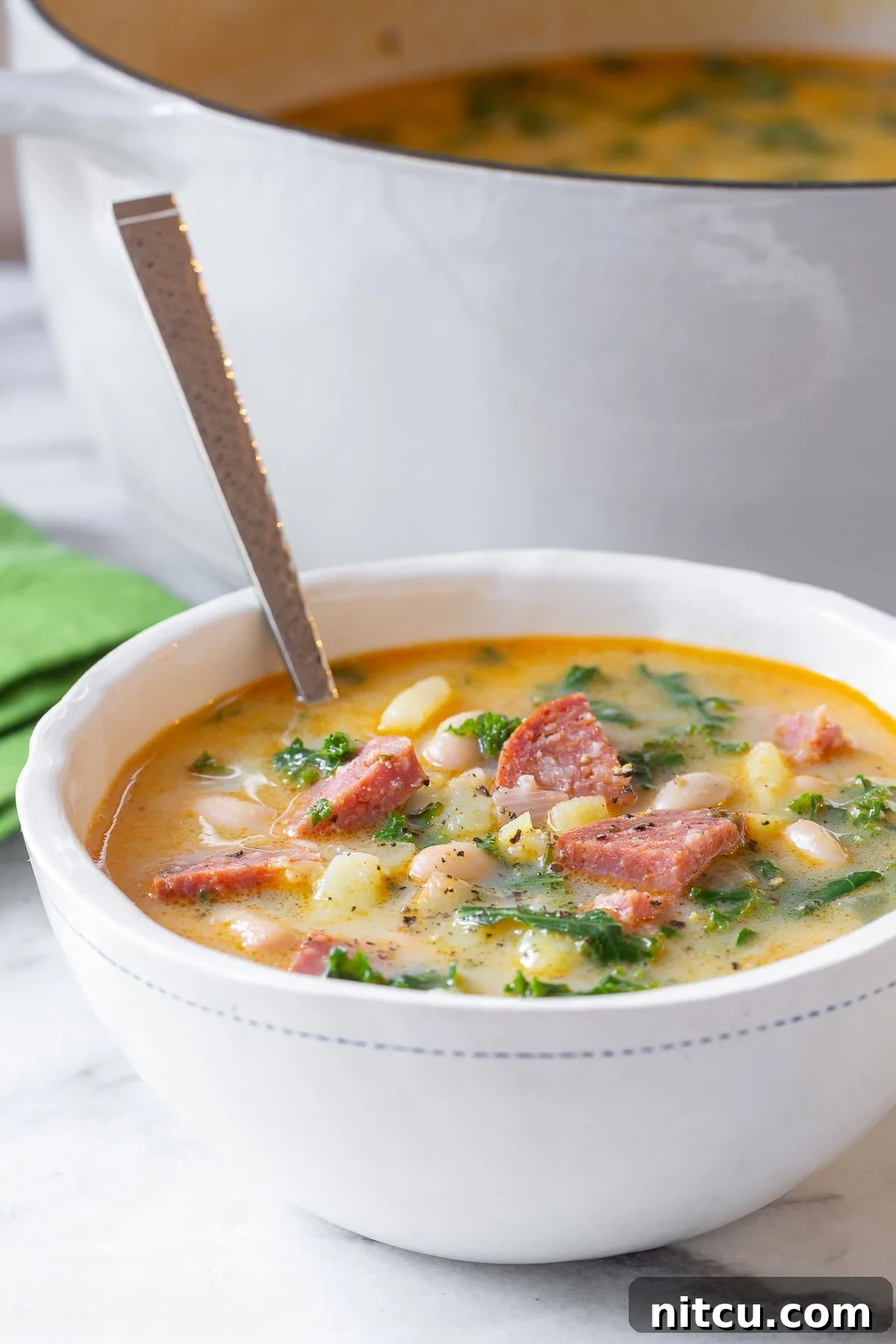 Two white bowls filled with hearty sausage and kale soup, a delicious Caldo Verde meal.