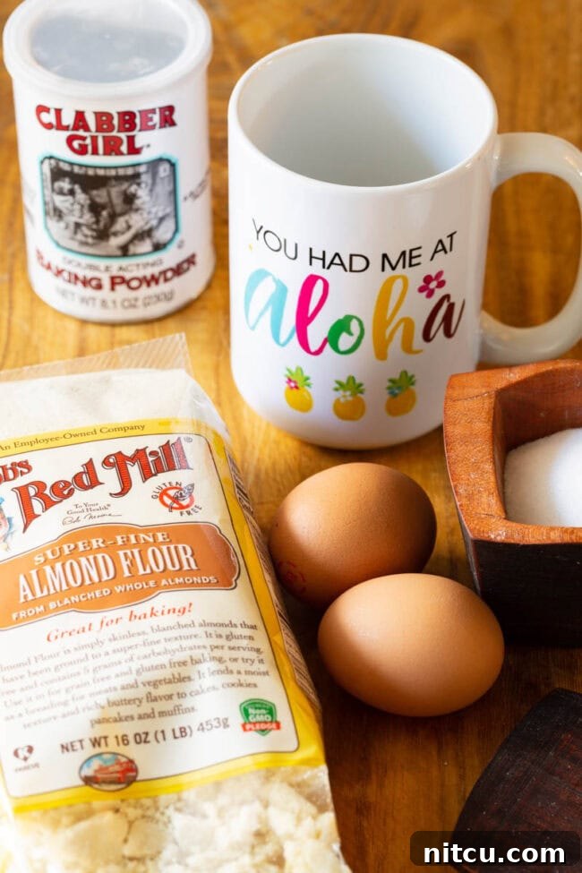 A white mug, container of baking powder, bag of almond flour, two eggs, and a wood bowl of salt.