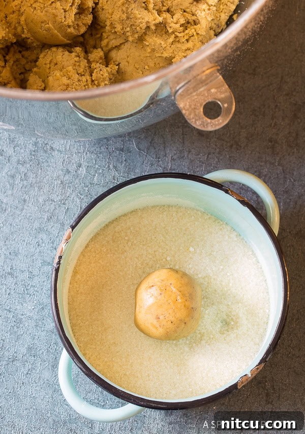 Brown butter cookie dough balls being rolled in granulated sugar.