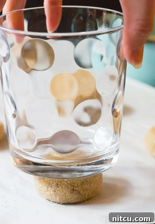 A drinking glass pressing down cookie dough to flatten it before baking.