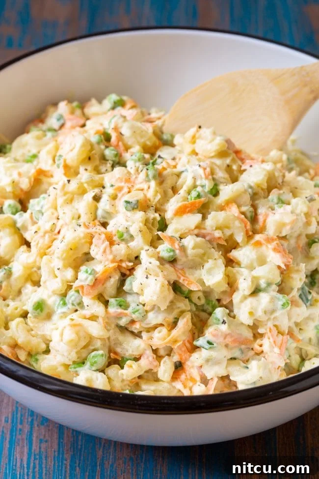 Bowl of potato and mac salad with a wooden spoon, showcasing the creamy texture and vibrant ingredients.