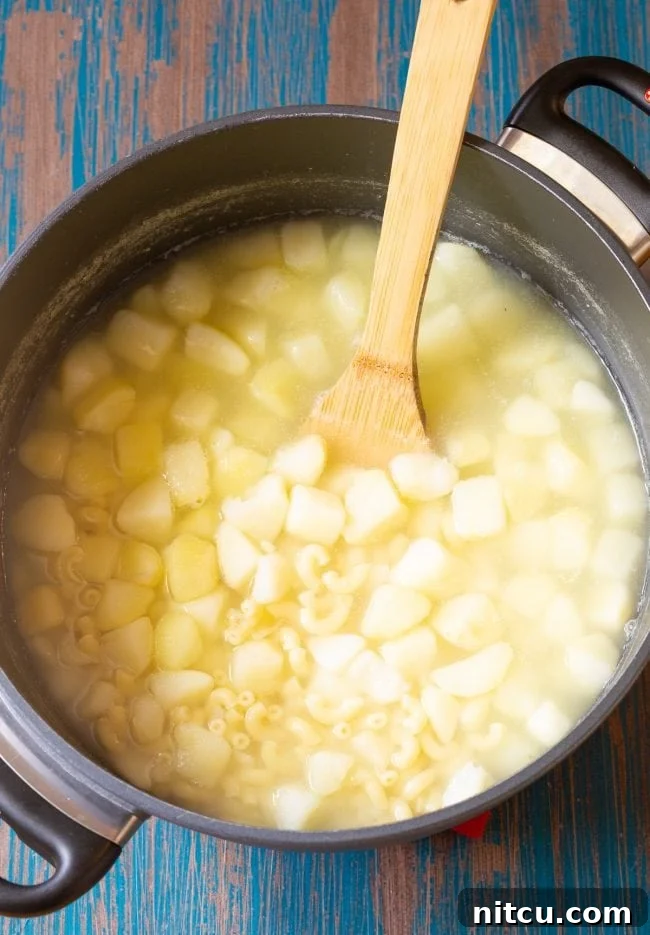 Pasta and potatoes boiling in a pot with a wooden spoon, indicating the start of the cooking process.