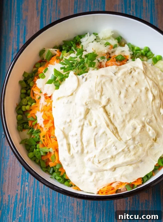 Ingredients for this potato pasta salad in a large mixing bowl with the dressing on top, ready to be mixed.