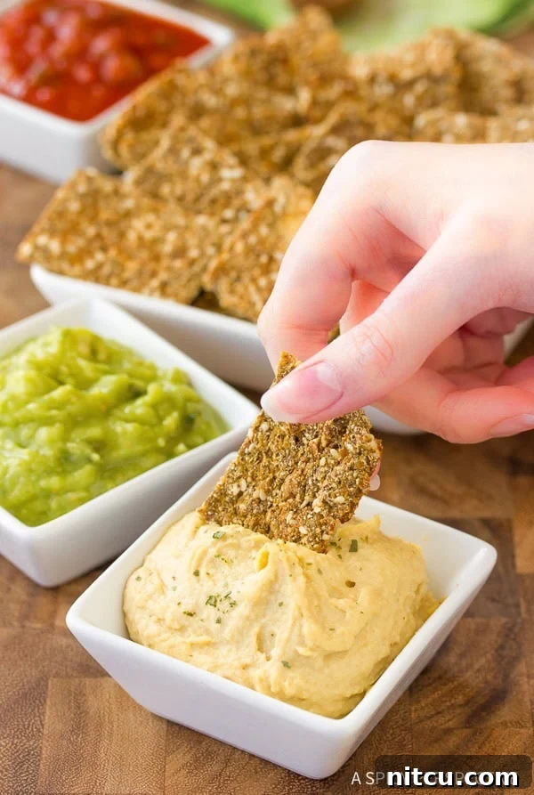 A hand dipping a golden cauliflower cracker into a small white bowl of creamy hummus, highlighting its perfect crunch and versatility.