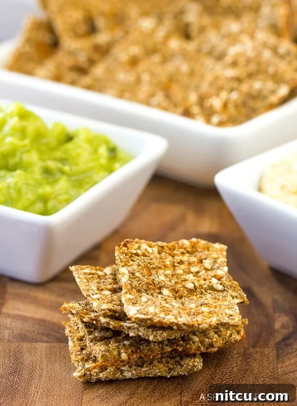 A vibrant stack of low carb cauliflower crackers arranged next to small white square dishes filled with various colorful dips, showcasing their perfect texture and serving versatility.