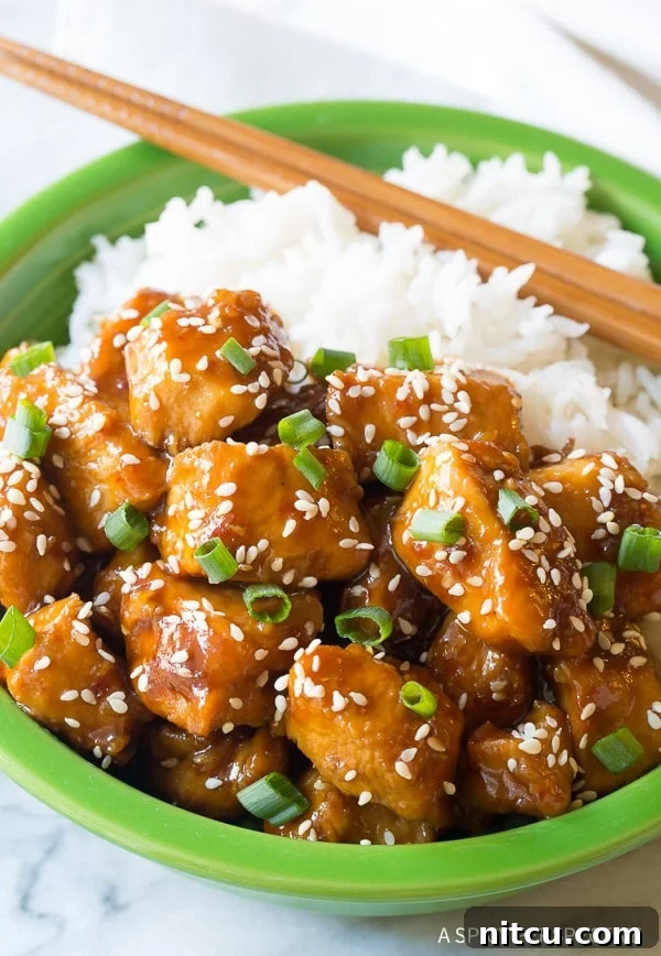 Instant pot sesame chicken in a bowl served with rice, garnished with sesame seeds and green onions.