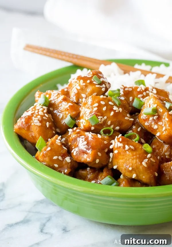 Chinese sesame chicken served in a vibrant green bowl with rice, garnished with sesame seeds and green onions.