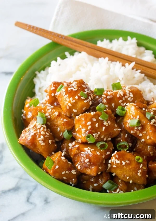Sesame chicken with rice in a green bowl, perfectly arranged with chopsticks on the side, ready to eat.