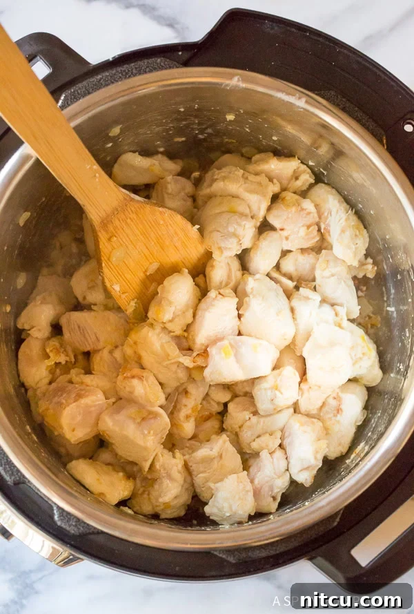Stirring pieces of cornstarch-coated chicken breasts with a wooden spoon in an Instant Pot, browning them gently.