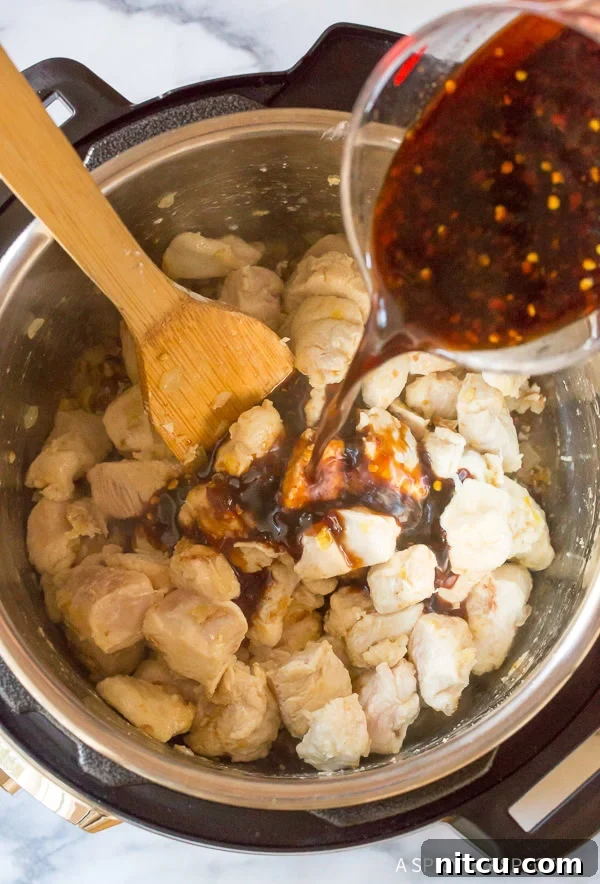 Adding the sweet and spicy sesame sauce mixture to the chicken pieces in an Instant Pot, ensuring even coating.