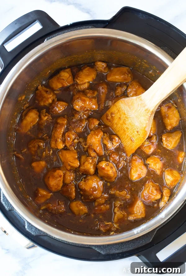 Stirring sticky chicken pieces in an Instant Pot, showing the sauce thickening and clinging to the chicken.
