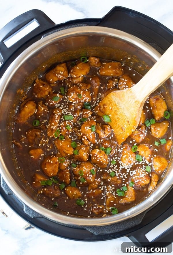 Adding a generous sprinkle of sesame seeds and fresh green onions to the cooked chicken in an Instant Pot for garnish.