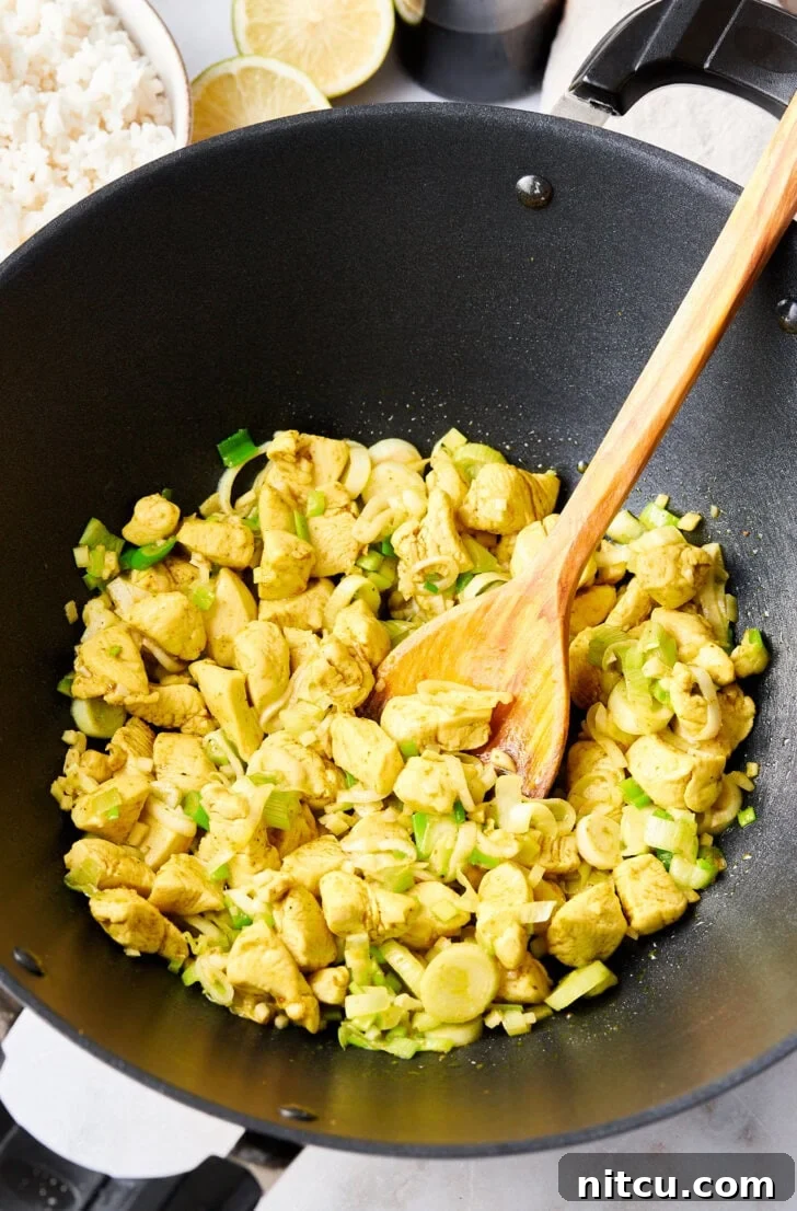 Sautéed chicken and vegetables sizzling in a large skillet, building the flavor base for the fried rice.