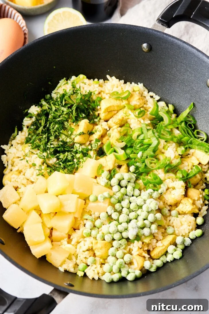 Colorful array of vegetables for Thai fried rice, expertly mixed in a large skillet, ensuring every component is perfectly cooked.