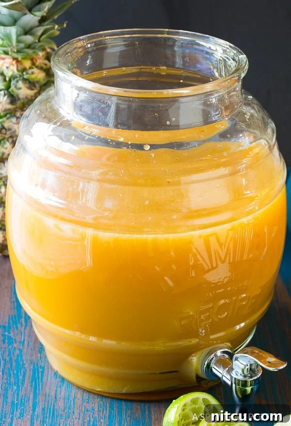 Refreshing Goombay Punch, a tangy large-batch Caribbean cocktail recipe, poured into a large glass dispenser ready for serving