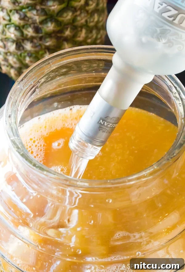 Pouring Goombay Punch ingredients into a large batch jug, showing the preparation of a Caribbean cocktail for a crowd