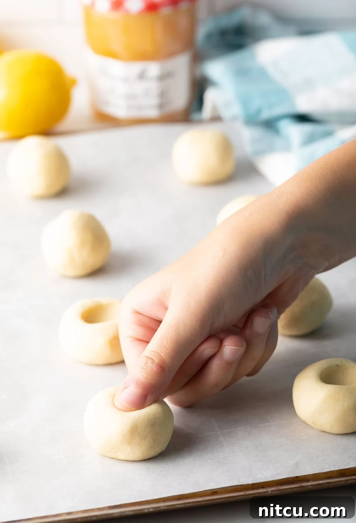 Sheet pan with the lemon thumbprint cookies dough balls and using a thumb to press the indents for the lemon custard