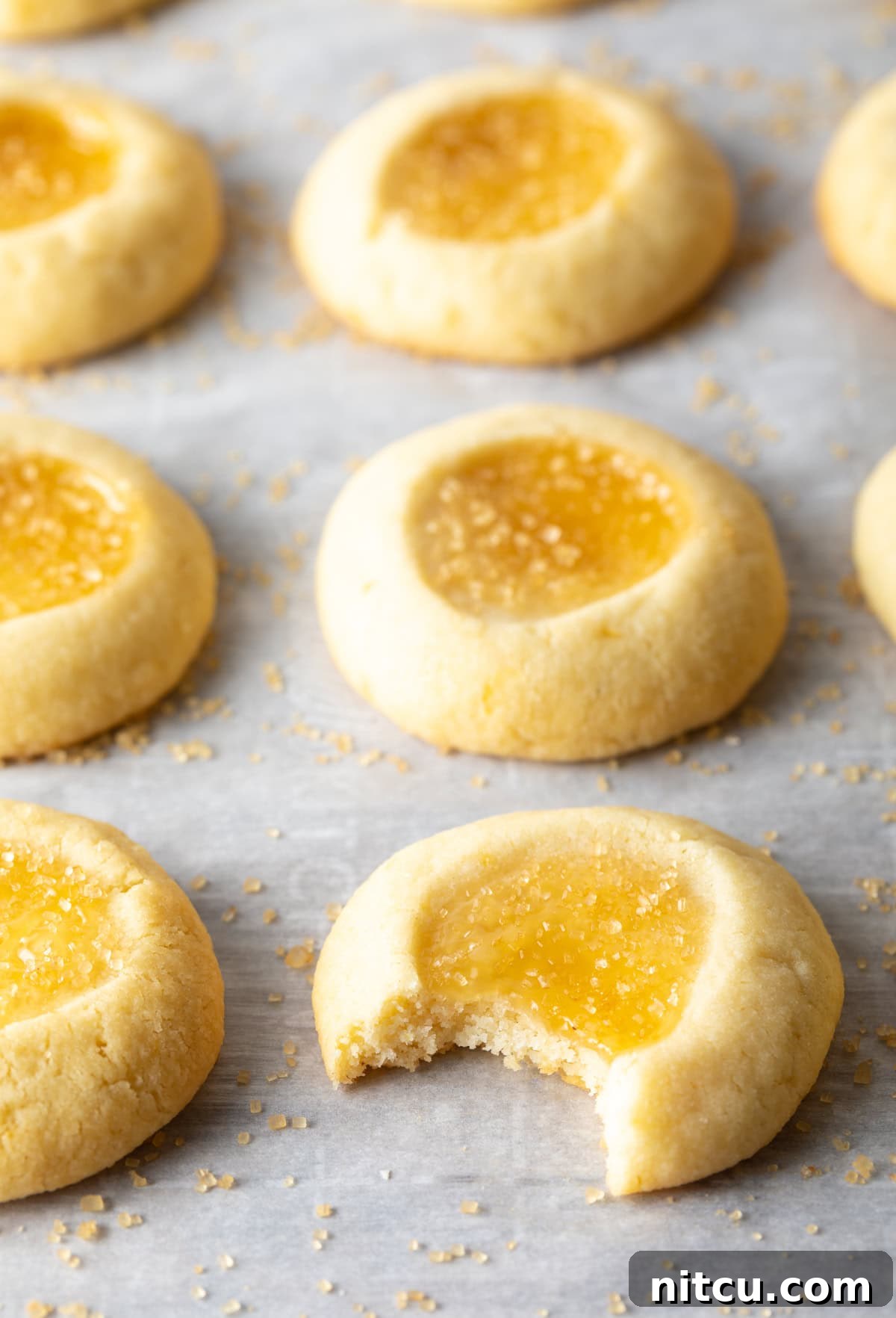 One lemon thumbprint cookie has a bite taken out of it laying on the baking sheet with the others
