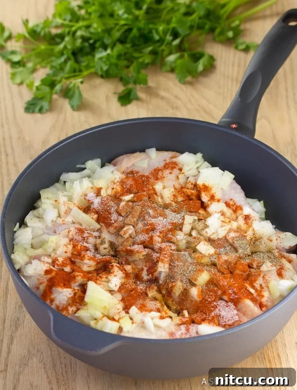 Chicken Paprikash simmering in a skillet with chopped onions and vibrant paprika