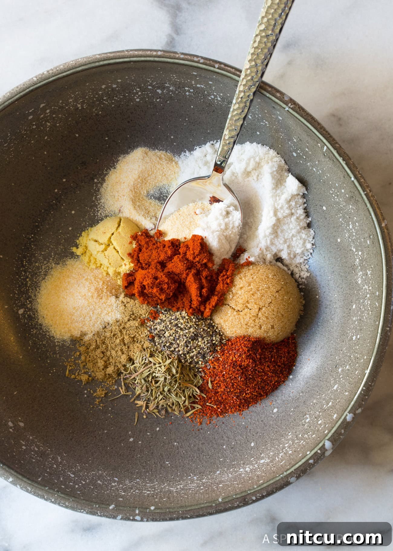 A small white bowl filled with a rich, vibrant blend of herbs and spices, showcasing the key ingredients for homemade steak seasoning.