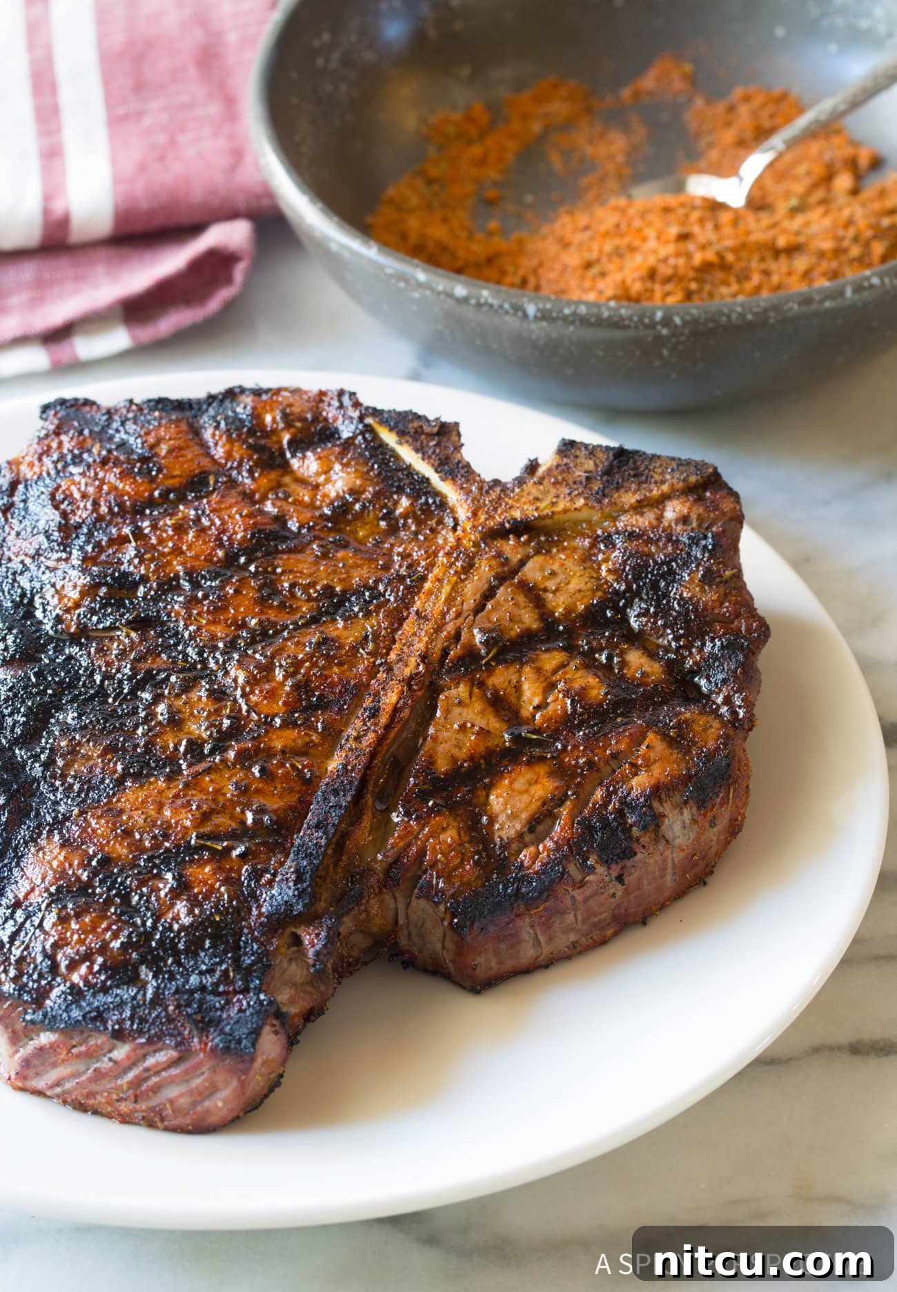 A perfectly grilled steak on a white plate, with a small bowl of the homemade steak seasoning in the background, ready to be served.