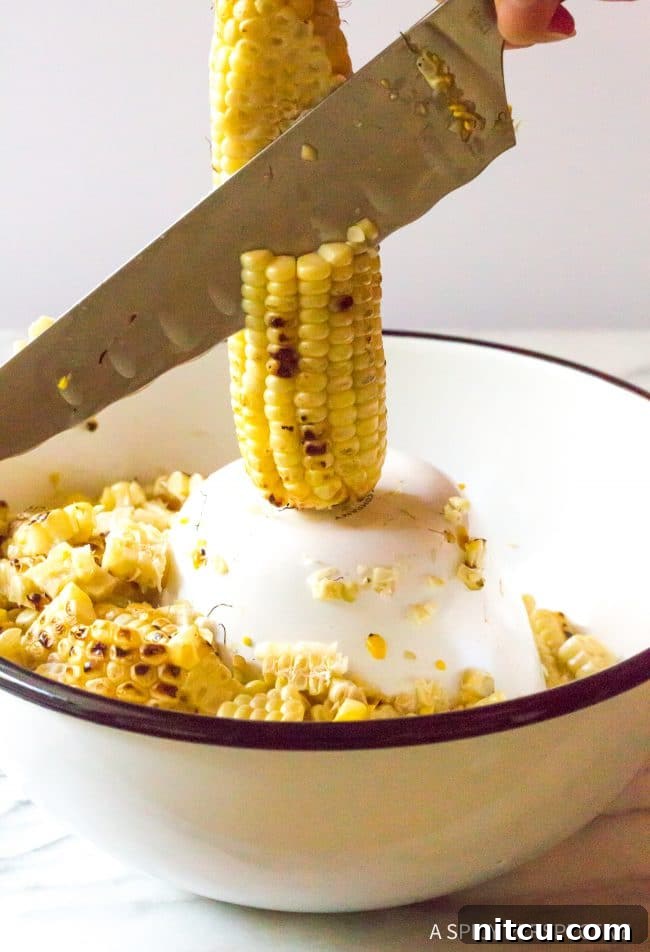 Closeup of a knife expertly removing corn kernels from the cob into a bowl, demonstrating the technique for preparing esquites.