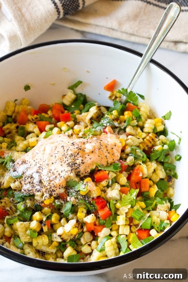 Creamy salad dressing being gracefully tossed into the colorful street corn salad ingredients, ensuring even coating.