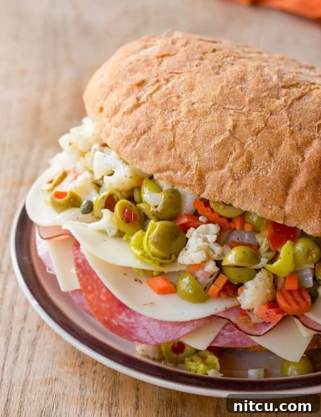 A generously filled New Orleans Muffuletta Sandwich, sliced and served on a rustic plate, showcasing layers of deli meats, cheeses, and a vibrant olive salad.