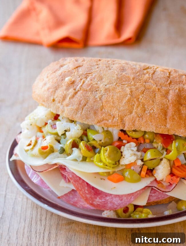 An absolutely incredible New Orleans Muffuletta Sandwich, expertly sliced and arranged on a plate, ready to be devoured, highlighting its abundant layers and enticing olive salad.