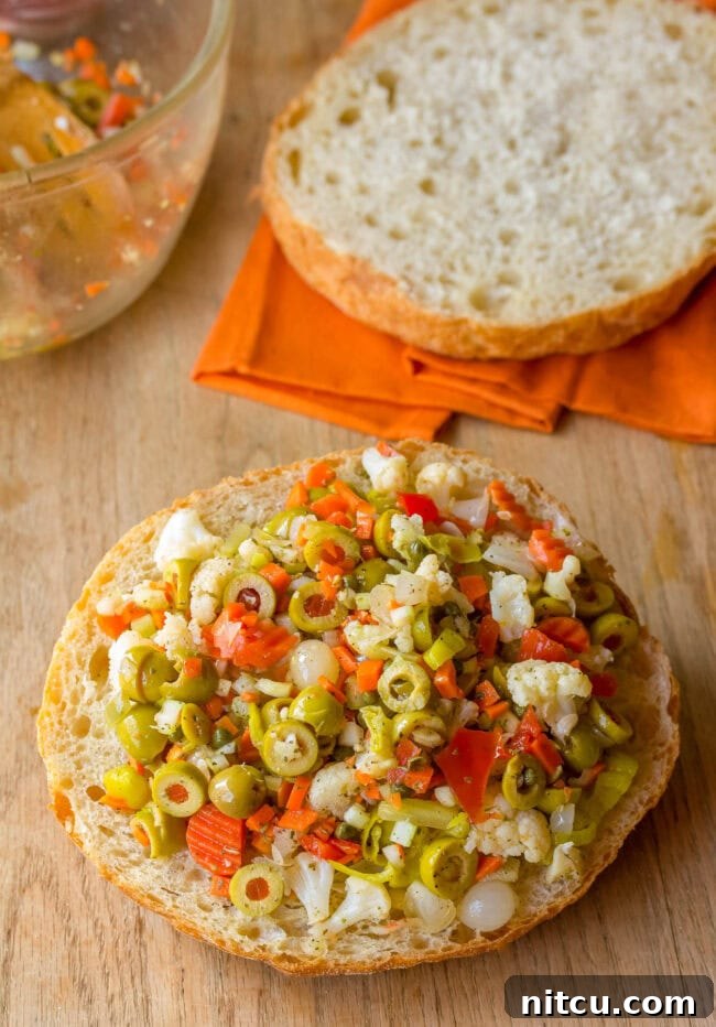 The first layer of creamy provolone cheese being placed on the bottom half of a round Italian bread loaf for a New Orleans Muffuletta sandwich.