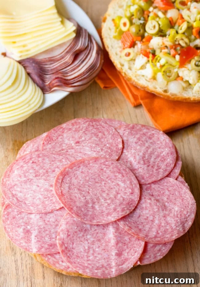 Slices of salami being carefully arranged over the ham and provolone, adding another robust flavor to the growing sandwich.