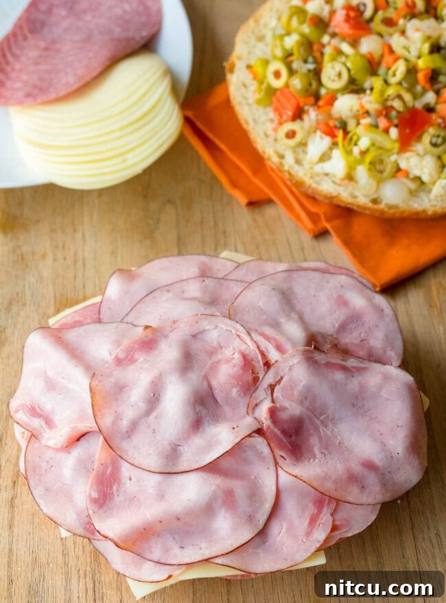 The vibrant, chunky Muffuletta olive salad being generously piled high on top of the layered meats and cheeses.