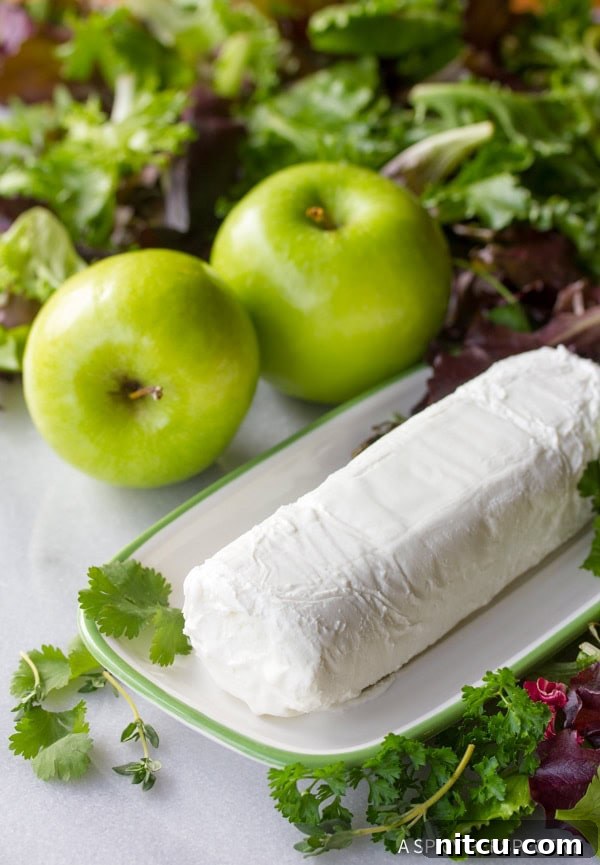 A log of goat cheese on a wooden cutting board, with two green Granny Smith apples in the background.